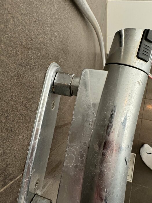 Närbild på duschblandarens fästen mot en kaklad vägg, med stor och liten mutter synlig.