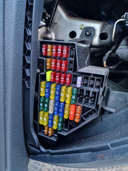 Öppen säkringslåda i bil med flera färgade säkringar i olika amperevärden.