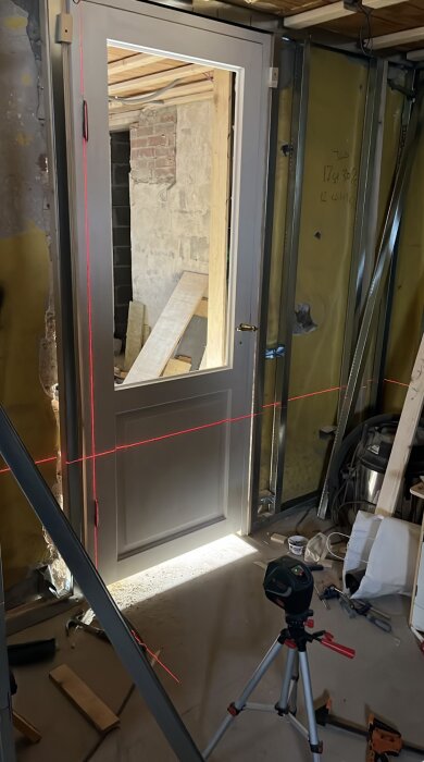 Källarrenovering med installation av innerdörr, omringad av stålreglar och en laserljusnivå framför dörren.