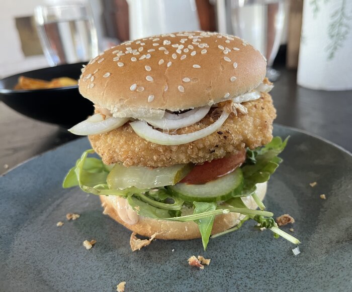 Kycklingburgare med sallad, tomat, lök och sås serverad på en tallrik.