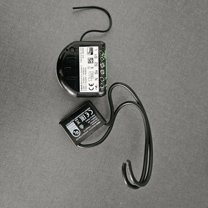 Elektrisk transformatorpuck för belysning med anslutna kablar på en grå yta.