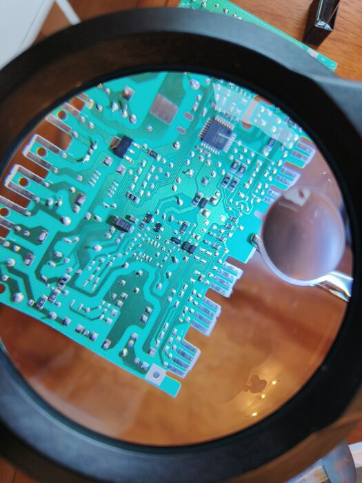 Kretskort sett genom förstoringsglas med synliga elektroniska komponenter och lödningar.
