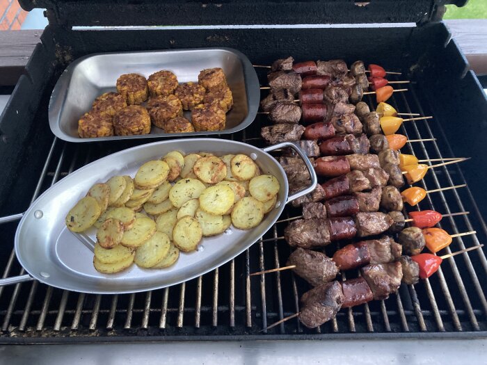 Grillad mat på grillen inklusive köttspett, korvar, marinerade grönsaker och stekt potatis.
