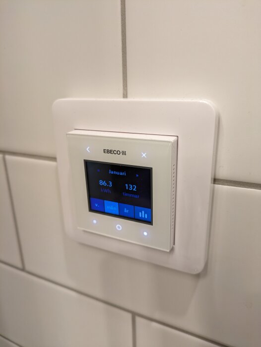 Värmesystemets displayvisare visar förbrukning 86,3 kWh i januari, monterad på vit kakelvägg.