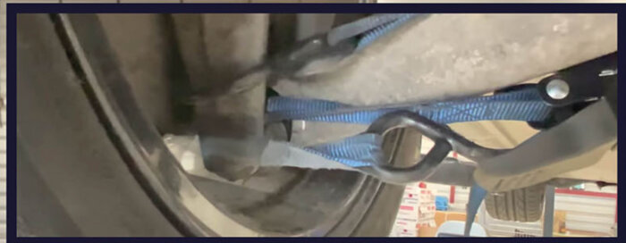 Närbild på en blå stödkabel fäst vid en sprucken länkarm på en bil under reparation.