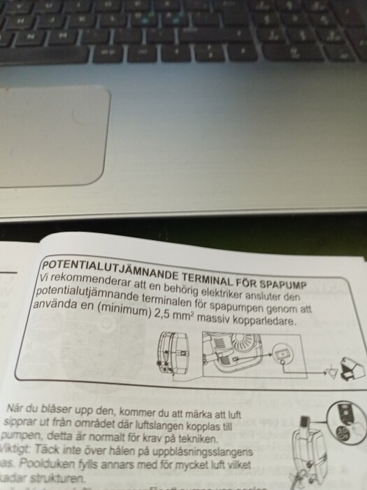 Manual med diagram och instruktioner för anslutning av en potentialutjämnande terminal, vilande på ett laptop-tangentbord.