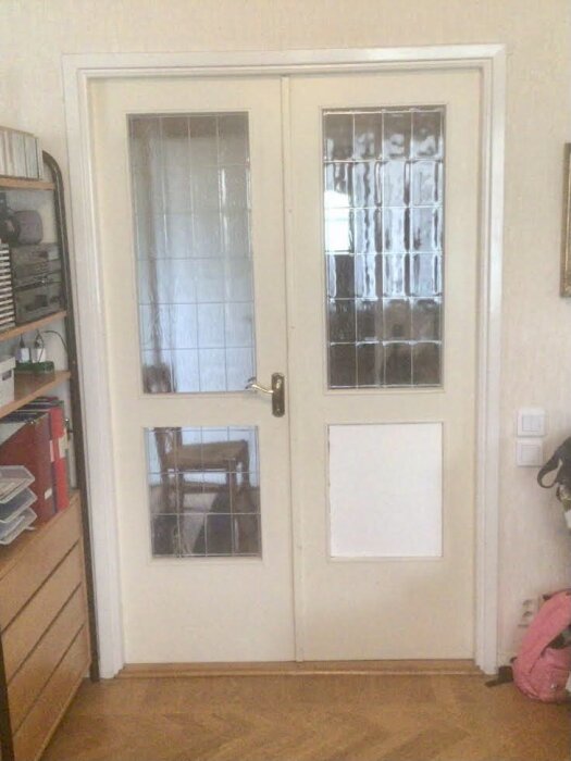 Dubbeldörrar med en frigolitskiva ersättande en trasig glasruta i den ena dörren.
