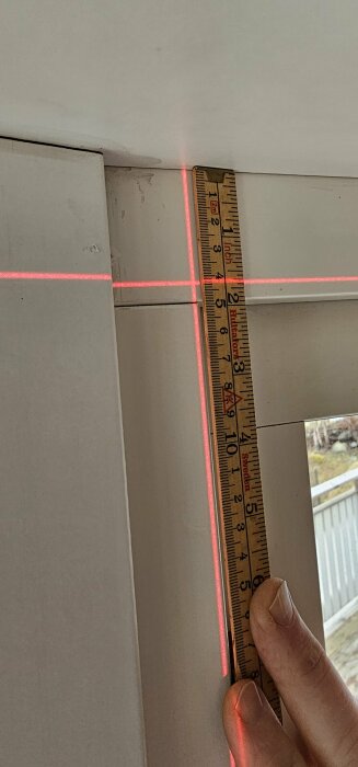 Mätning av ojämn balkongdörr där en linjelaser visar en nästan en centimeters skillnad i höjd.