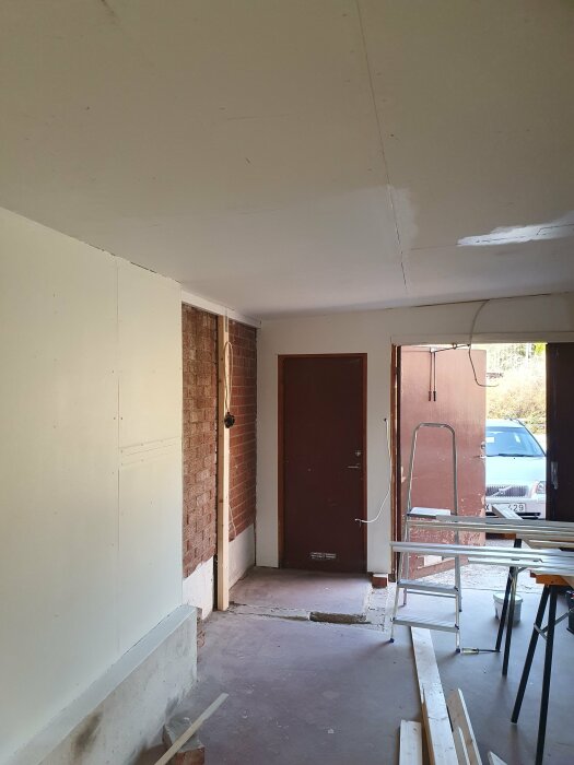Interiör av garage under renovering med nymålade väggar och listverk, oanvända lister på golvet.