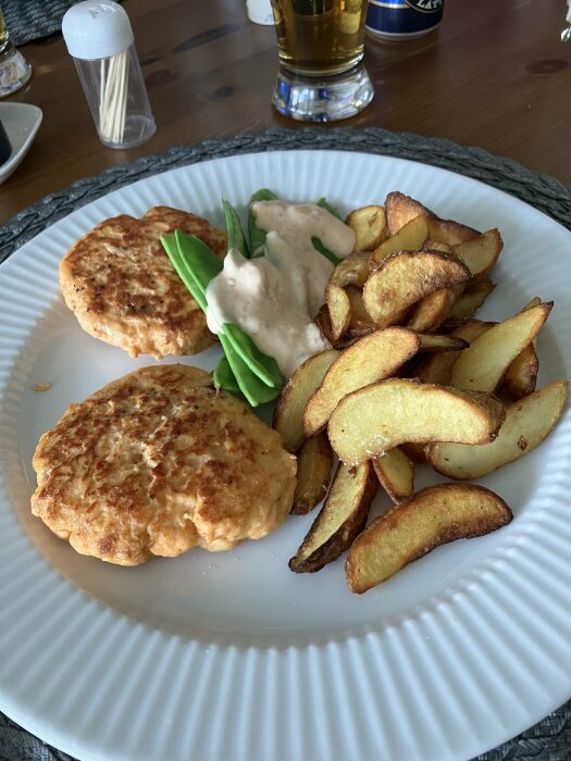 Laxburgare på tallrik med potatisklyftor, sockerärtor och sås vid en dukad bordsservering.