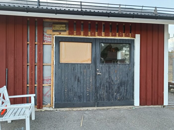 Ett garage med en befintlig gammal dörr, delvis demonterad, och synlig nivåskillnad mellan asfalt och golv.