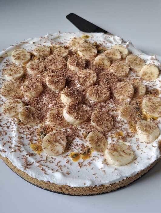 Banoffepaj med skivad banan och passionsfruktsås toppad med grädde och riven choklad.