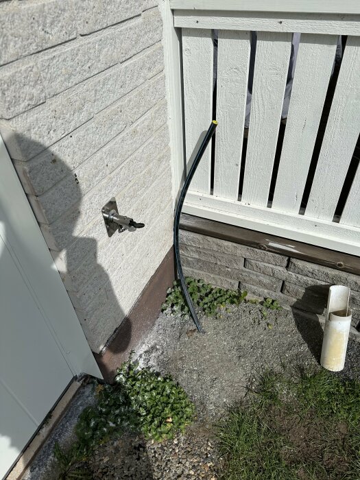 En trädgårdsslang kopplad till ett vattenutkast på en husvägg, i behov av korrekt koppling.