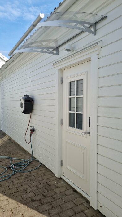 Transparent taköverbyggnad från Biltema monterad över en vit garagedörr på ett hus med ljus sidopanel.