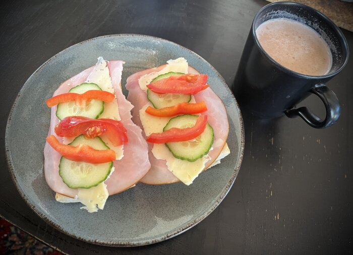 Frukost med skinkmackor toppade med ost, tomat, gurka och en kopp kaffe på grå tallrik.