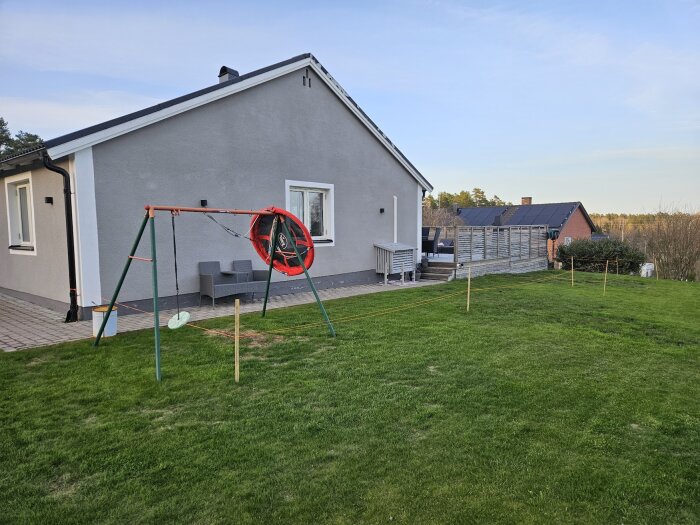 Husets baksida med gräsmatta, en befintlig altan och snören som markerar den planerade utbyggnaden av altanen.