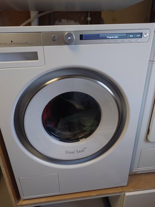 Frontal bild av en vit tvättmaskin med märkningen "Steel Seal" och kläder synliga i trumman.