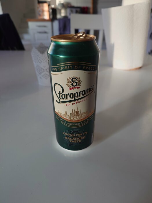 En Staropramen ölburk på ett vitt bord med köksbakgrund.