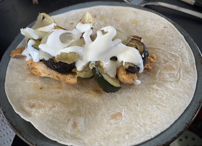 Wrap med kycklingstrimlor, ugnsrostade grönsaker och vitlökssås på en tallrik.