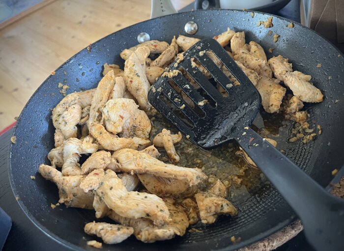 Stekt kycklingstrimlor i kryddig marinad i en stekpanna med en svart stekspade.