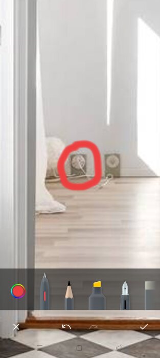 Gammalt teleuttag i utanpåliggande dosa markerat med röd cirkel på en vägg bredvid en dörr.