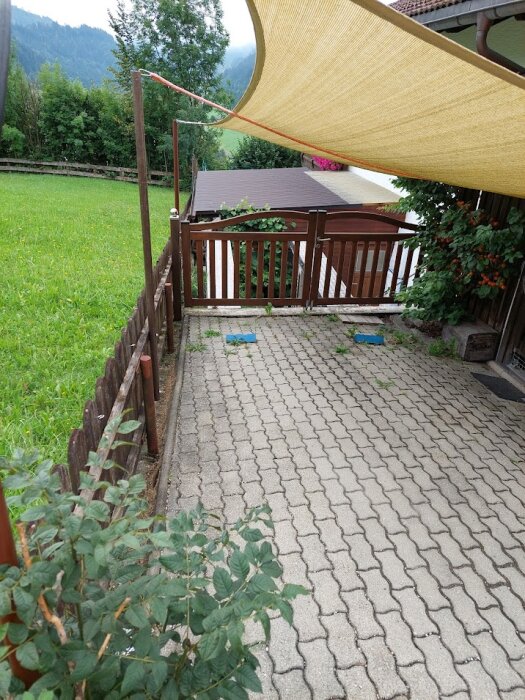 En uppfart med stenläggning och en brun trägrind öppen ut mot en gräsmatta.