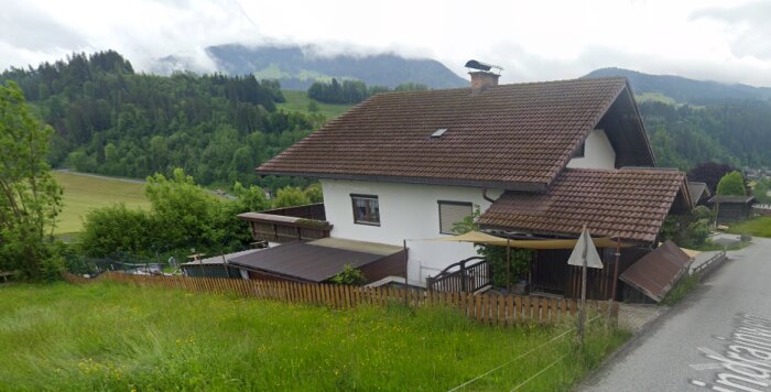 Ett hus vid en backe med kuperad terräng och dimmiga berg i bakgrunden.