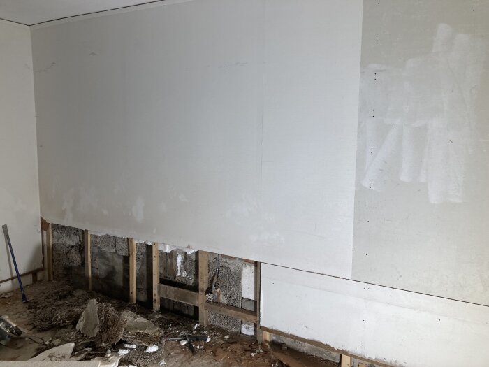 Renoveringsrum med avlägsnad väggsektion och exponerade träreglar efter en vattenskada.