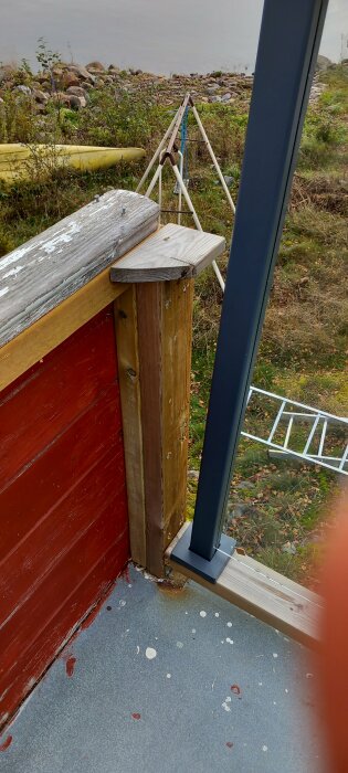 Monterat glasräcke med stolpfäste på trätrall nära havet och en gul kanot i bakgrunden.