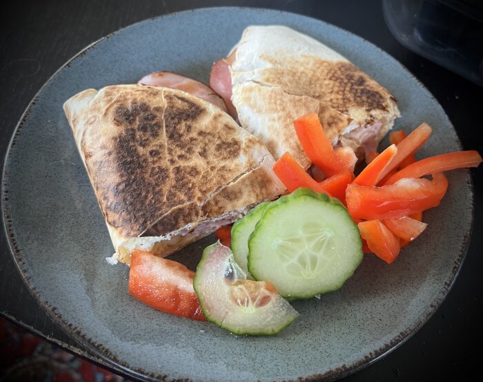 Hemlagad frukostburrito med skinka och ost, serverad med färska grönsaksstickor på en grå tallrik.