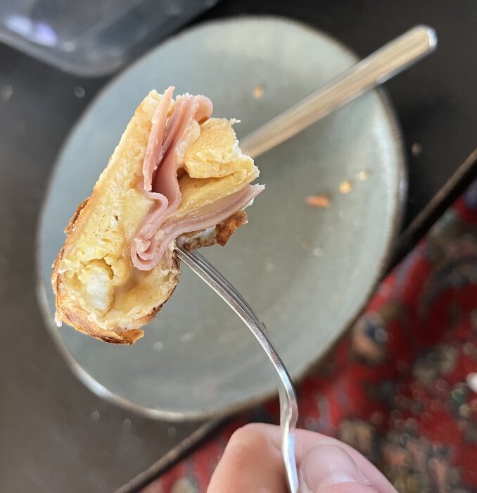 En frukostburrito med smält ost och rökt skinka på en gaffel framför en otydlig bakgrund.