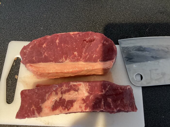 Ryggbiff med kappa på skärbräda bredvid en köttyxa, förberedelse för grillning.