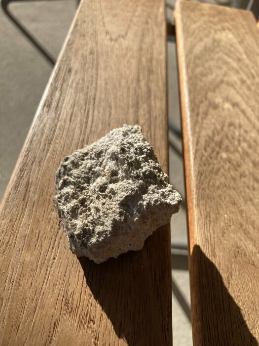 En bit grov sten placerad på en träbänk i solljus.