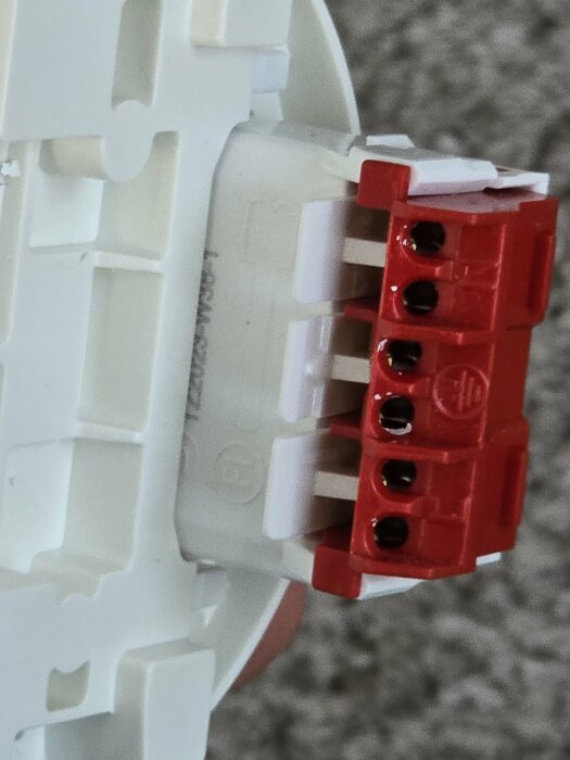 Närbild av en röd elektrisk dosa med ledningsterminaler installerade i en vit plasthållare.
