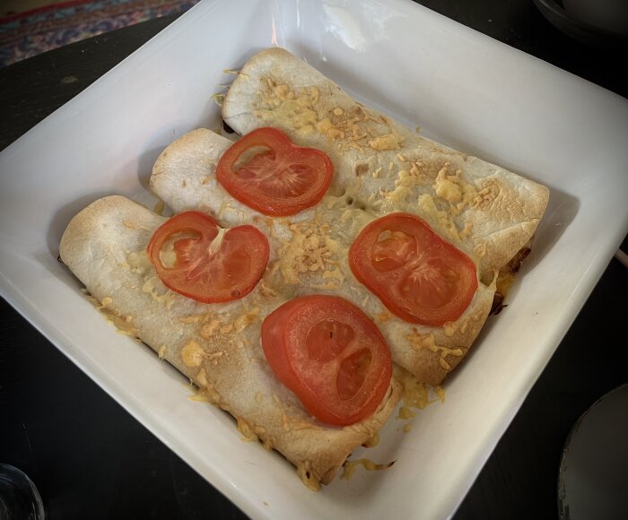 Tre värmda burritos med kyckling, ost och tomat i en vit form, serverade på bädd av sallad.