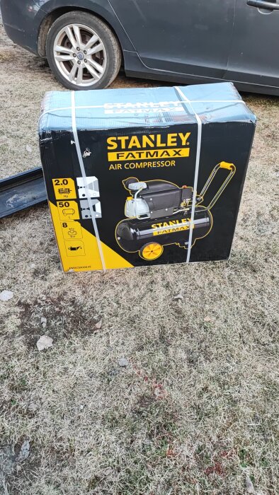 Oöppnad kartong med en Stanley Fatmax luftkompressor utomhus på gräsmark.