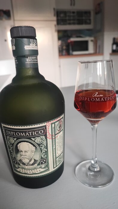 Flaska av Rom Diplomatico Reserva Exclusiva och ett glas med mörkt rom på köksbänk.
