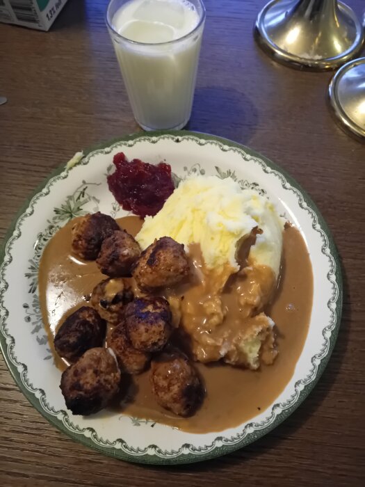 Tallrik med svenska köttbullar, potatismos, brunsås och lingonsylt, bredvid ett glas mjölk.