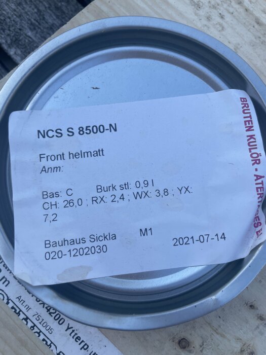Etikett på burk med texten "NCS S 8500-N, Front helmatt" och blandningskoder, liggande på ett träunderlag.