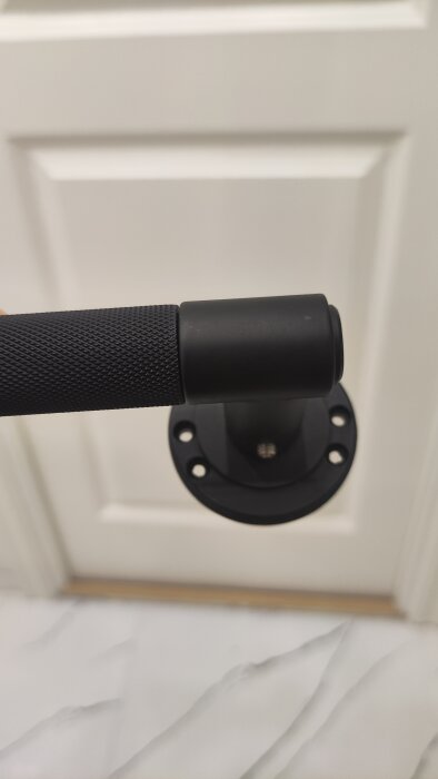 Nytt dörrhandtag med svart bas och texturerat grepp som inte passar standard låshus på vit dörr.