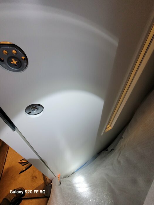 Närbild av en vit dörr med en synlig cirkelformad bula och belysning som framhäver defekten.