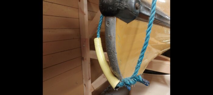 Böjd aluminiumskena fäst vid en kanots stäv med blått rep, söker liknande skena för reparation.