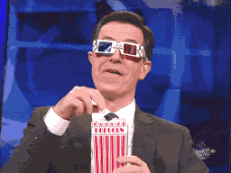 Man i kostym äter popcorn och bär anaglyph 3D-glasögon, ser underhållen ut.