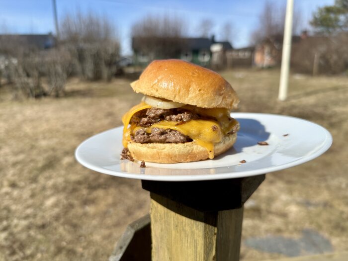 Hemmagjord smashburgare med ost och lök på en vit tallrik utomhus.