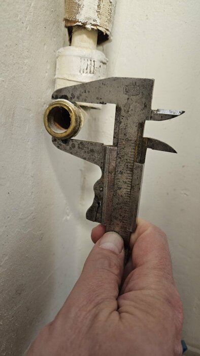 Hand som håller en skjutmått mot ett gammalt varmvattenrör för att mäta dess ytterdiameter.