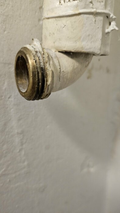 Gammalt vitmålat varmvattenrör med gängad ände för koppling i tvättstuga.
