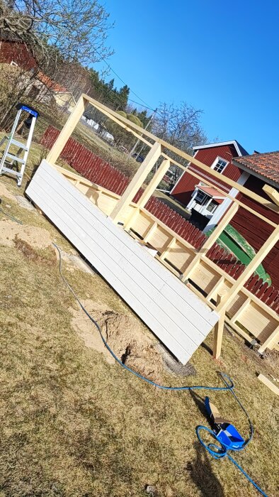 Halvfärdig trästomme för byggprojekt med nyinstallerad vit panel och en stege på växande gräsmatta.