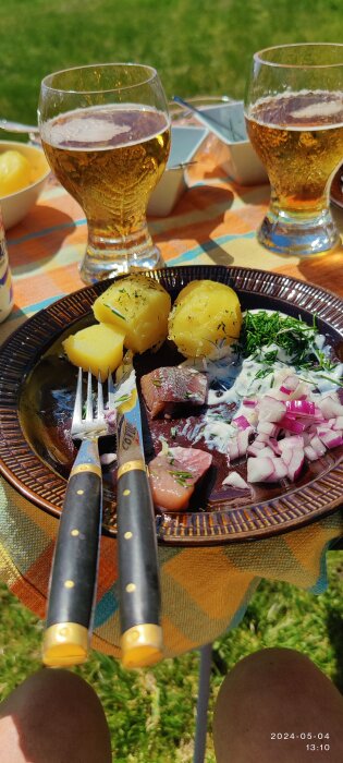 En tallrik matjessill och kokt potatis med rödlök och gräddfil, och ett glas öl i solskenet.