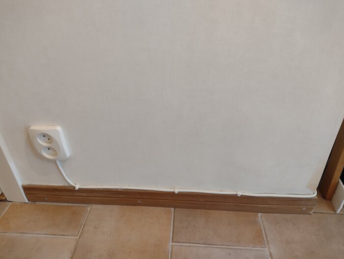 Elektrisk kabel löper längs med golvlisten och ett vägguttag i ett rum.