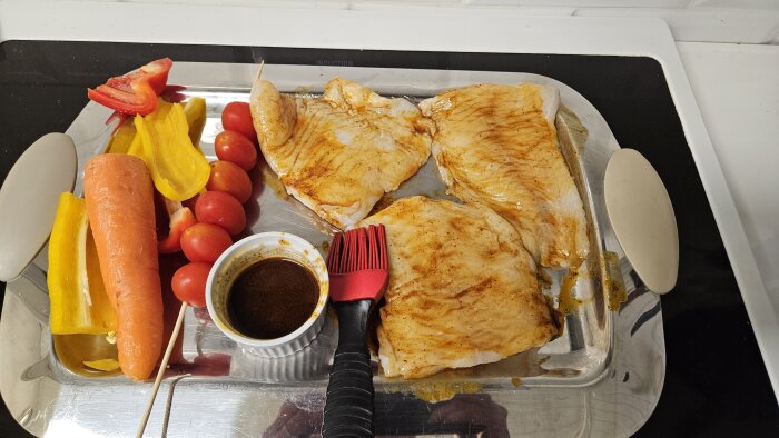 Grillade havskattsfiléer och grönsaker på ett ugnstråg med marinad och pensel.